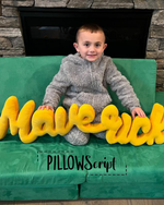 Load image into Gallery viewer, Child sitting on a green pillow with yellow custom PillowScript pillow with 'MAVERICK' letters, fireplace in the background.
